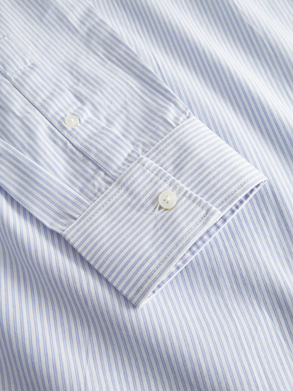 Close-up of Gabbas Sven Reg. Form LS - White Stripe, a premium, yarn-dyed, light blue and white striped dress shirt. It features vertical pinstripes, buttoned cuffs, and is made from 100% cotton with classic white buttons for an elegant look.