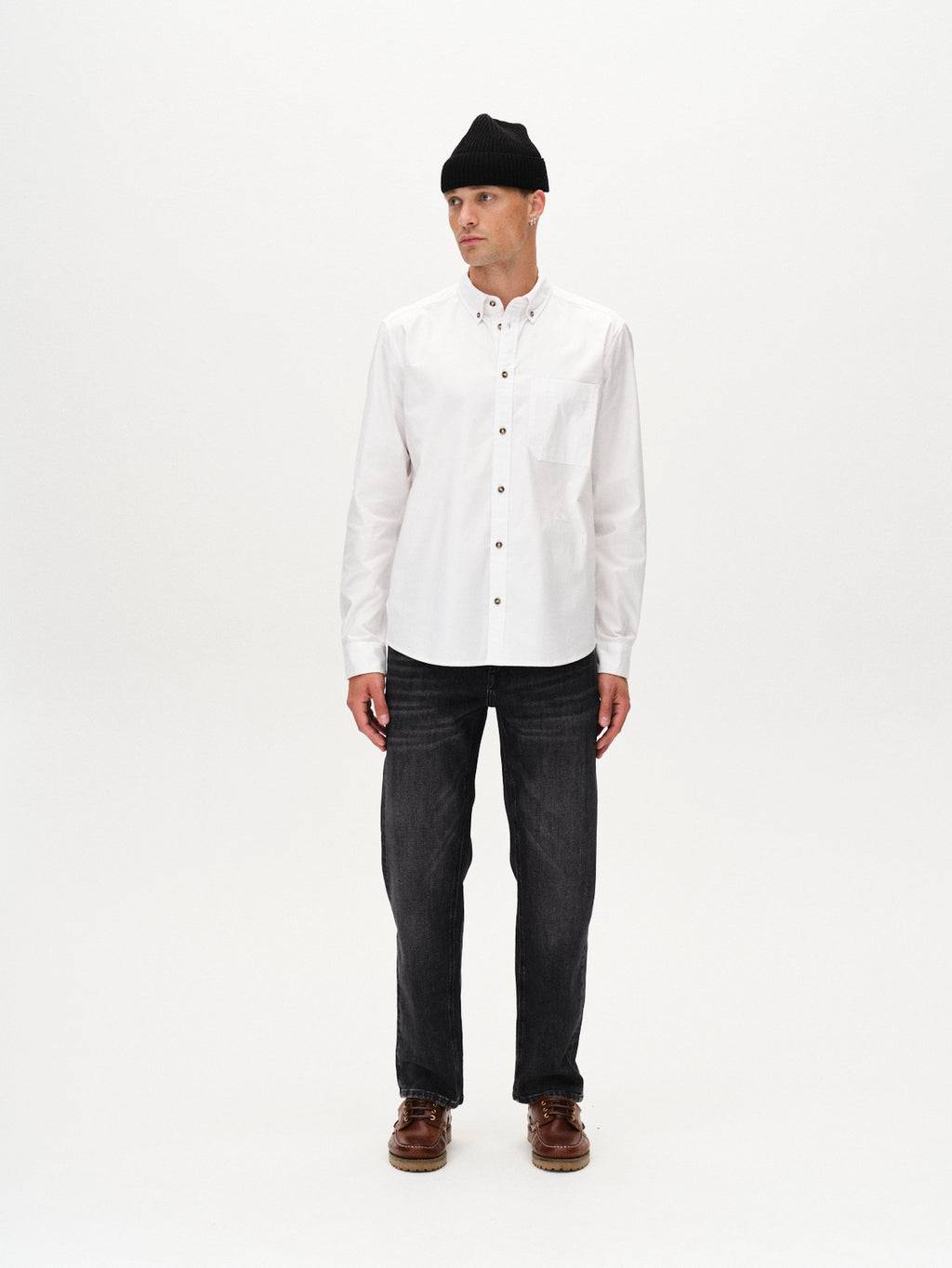 A man wears the Gabba Bent Reg Ox LS - White shirt, styled with a black beanie, dark jeans, and brown shoes, standing facing forward against a plain white background.