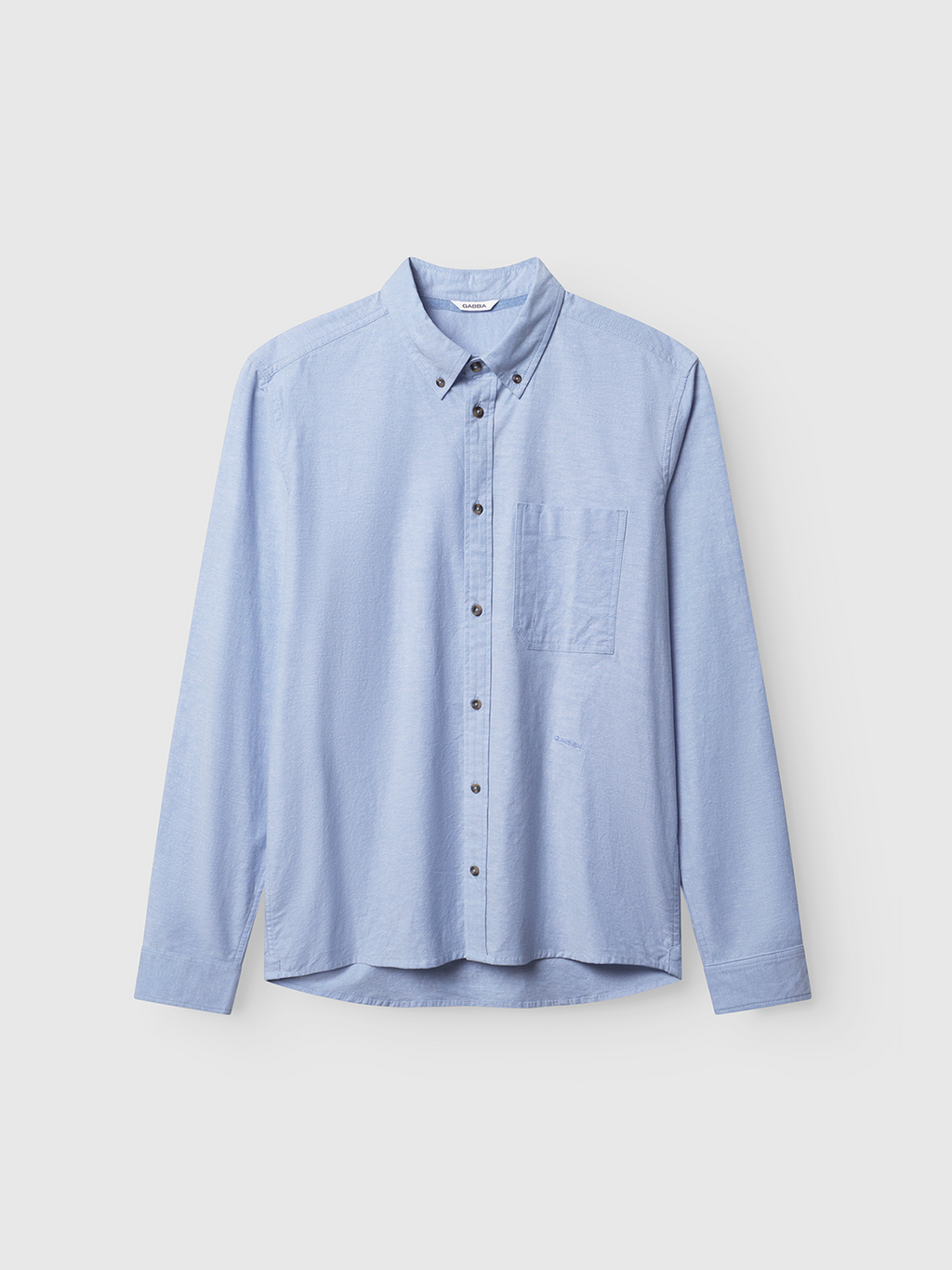 The Gabba Bent Reg Ox LS in light blue is a cozy, long-sleeved cotton shirt with a classic collar, dark buttons, and a small chest pocket. Displayed on a plain white background, it embodies timeless style and comfort.