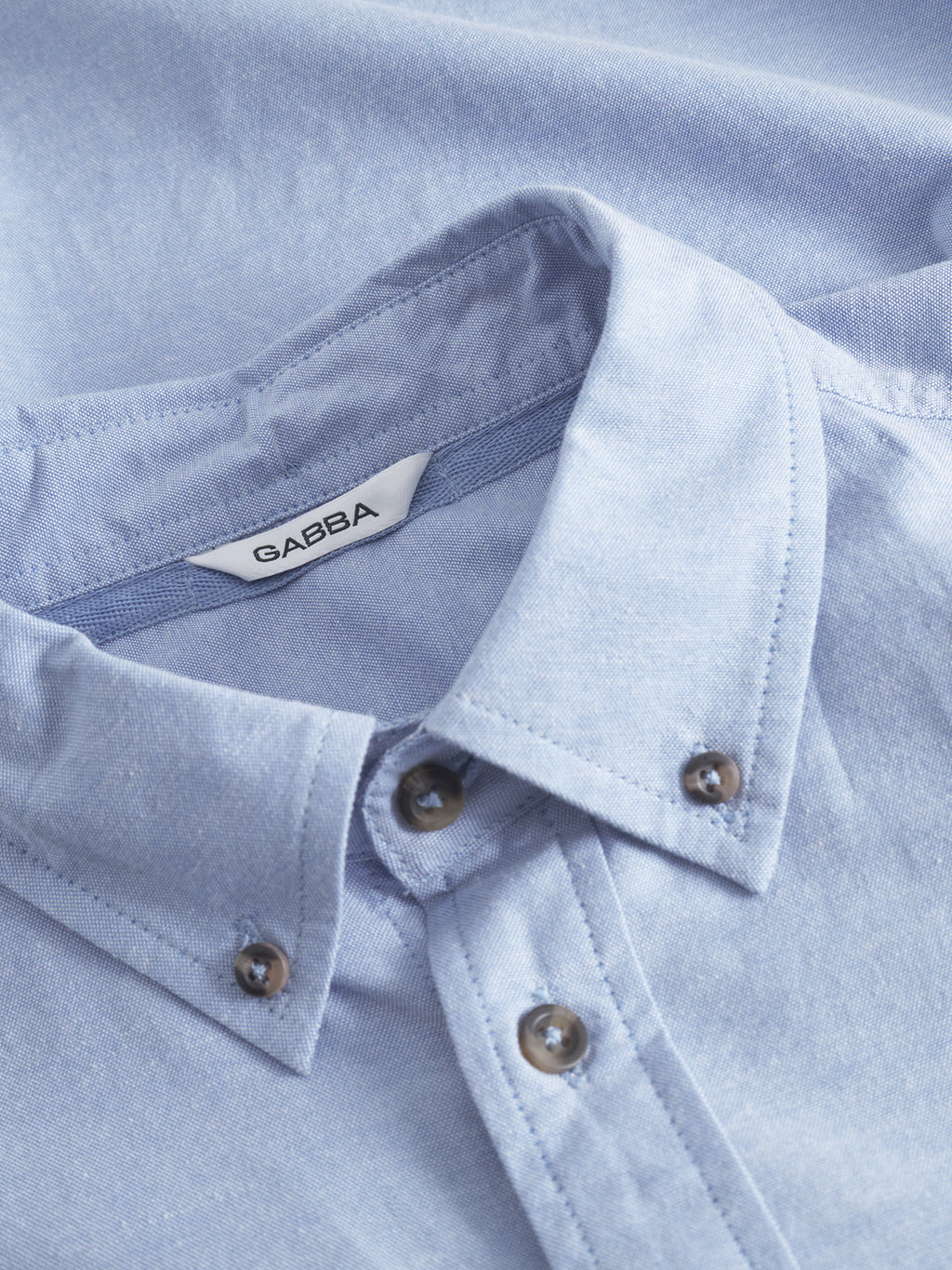 A close-up of the Bent Reg Ox LS - Light Blue cotton shirt from Gabba features a button-down design, with the brands tag inside the collar. The textured fabric adds depth and guarantees all-day comfort.