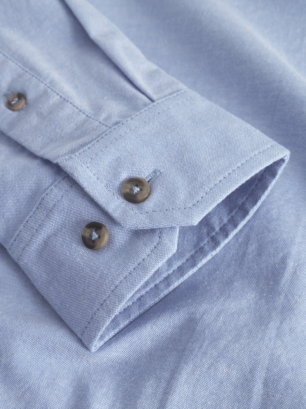 Close-up of Gabbas Bent Reg Ox LS - Light Blue shows a textured cotton cuff with two brown buttons, highlighting the subtle stitching and fabric for all-day comfort.