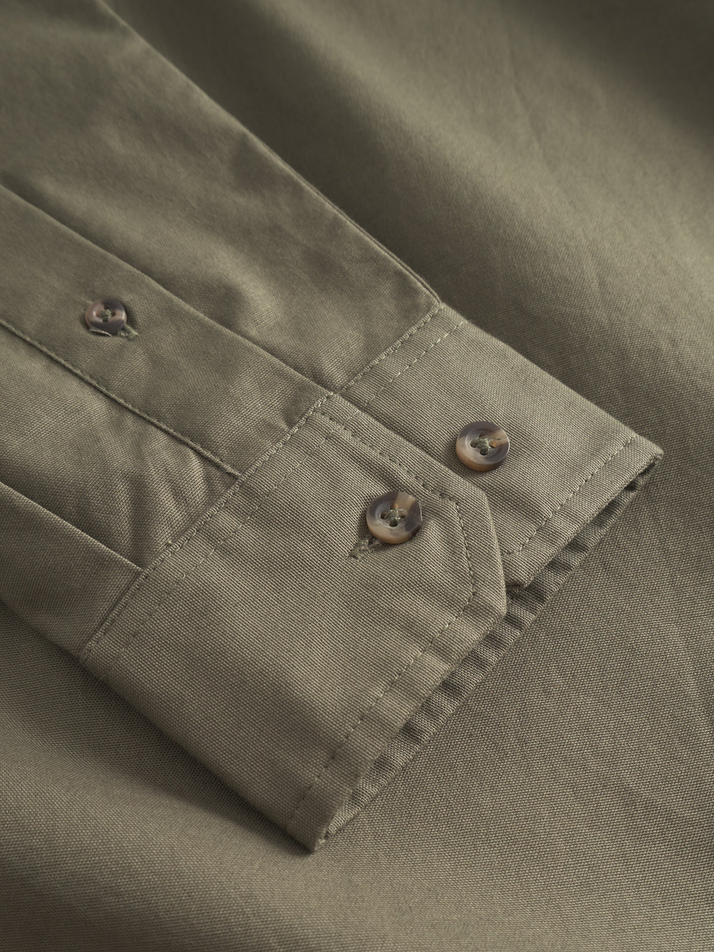 Close-up of a Bent Reg Ox LS - Army shirt sleeve by Gabba featuring a timeless design. The cuff, adorned with two marbled buttons, enhances the smooth fabrics texture, ensuring all-day comfort.