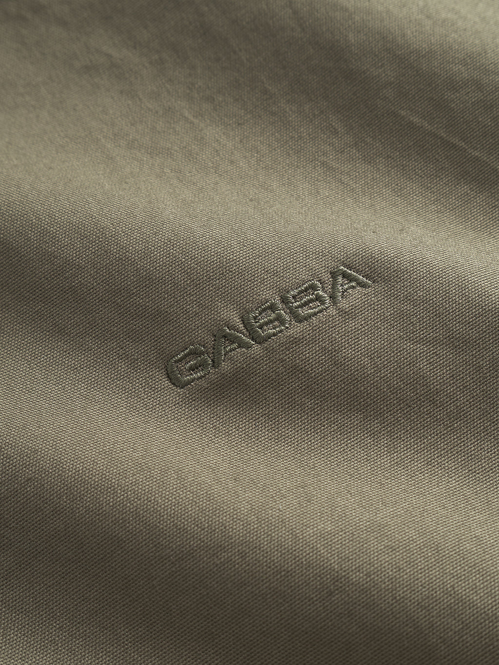 This close-up of the Bent Reg Ox LS - Army by Gabba showcases exquisite embroidery with GABBA in matching thread on smooth, olive green fabric. The piece not only offers all-day comfort but also a sophisticated textured look, making it a timeless design statement.