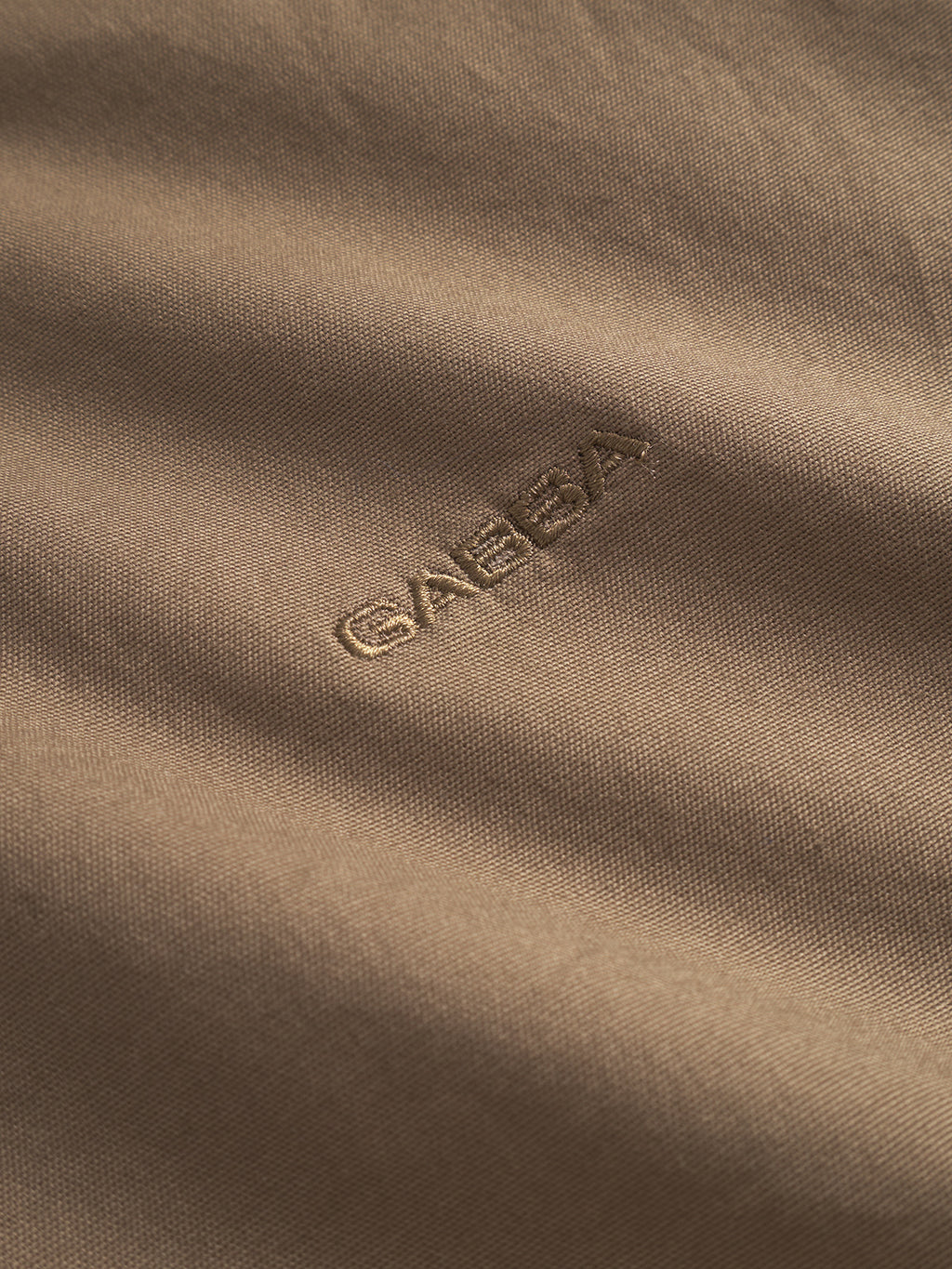 A close-up of Bent Reg Ox LS - Brown fabric displays the word Gabba in a slightly darker thread for subtle contrast. The smooth, gently rippled texture makes this versatile cotton shirt ideal for both formal and casual settings.
