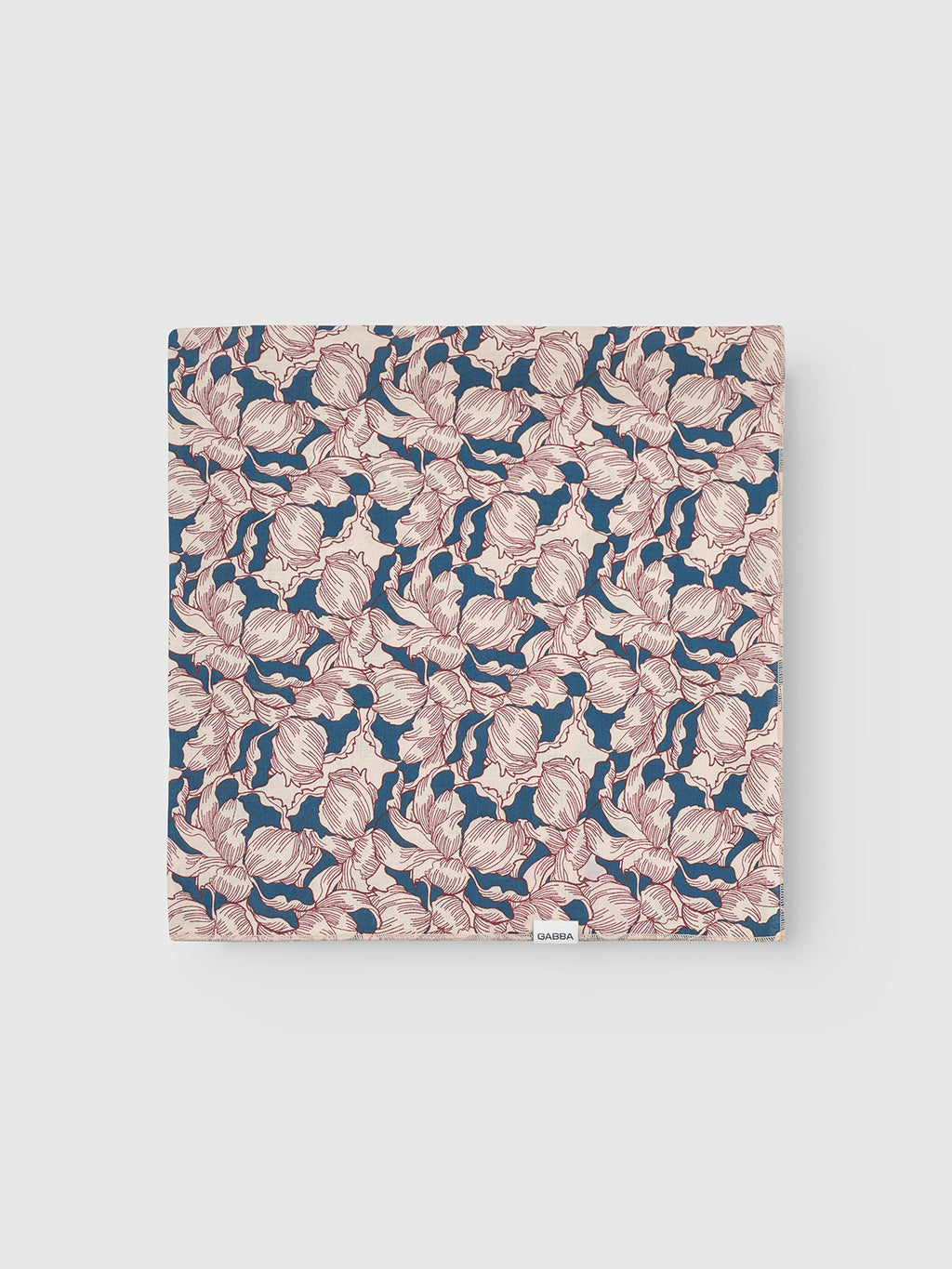 The Gabba Bandana Epo - Blue Pattern features a folded cotton piece with retro beige and pink flowers on a dark blue background, complete with a small white label.