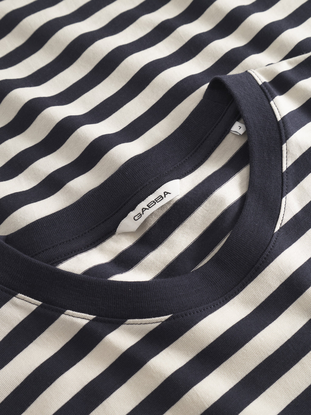 Close-up of a Navy Stripe t-shirt featuring horizontal stripes and a GABBA neck tag. Made from 100% organic cotton, the fabric is soft and neatly sewn, reflecting the quality of GOTS-certified craftsmanship.