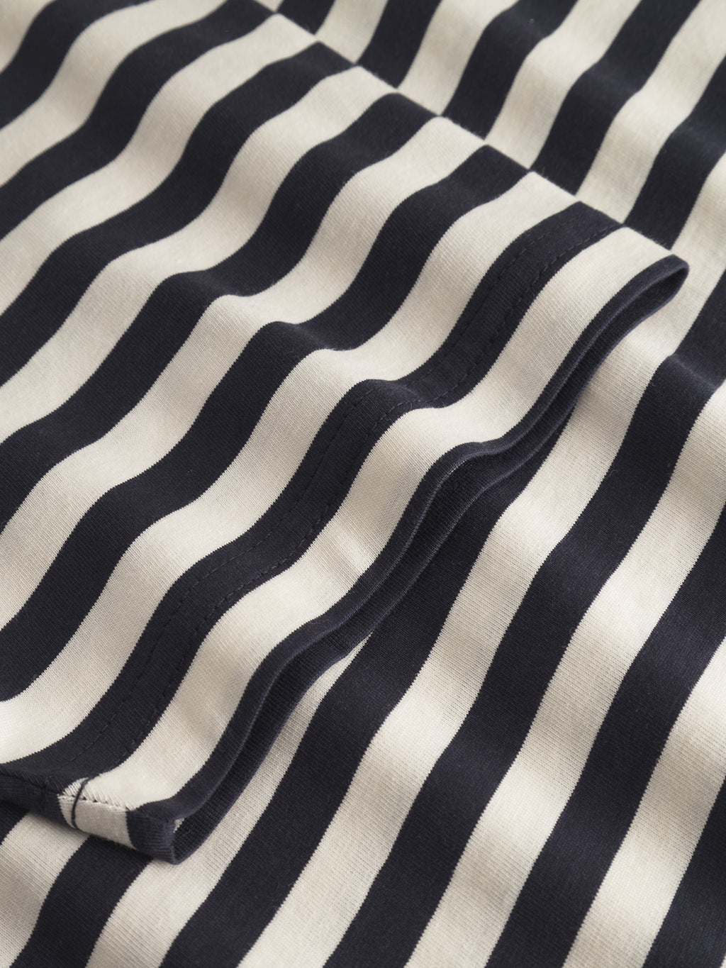 The Dune Logo Stripes SS GOTS - Navy Stripe by Gabba features a close-up of black and white striped fabric with wavy lines. Made from 100% organic cotton and GOTS-certified, the material is folded to create movement and depth.