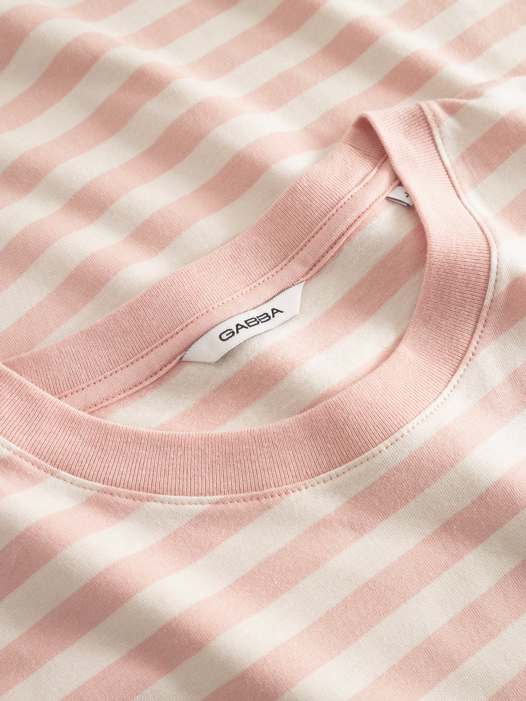 Close-up of Gabbas Dune Logo Stripes SS GOTS in rose stripes, featuring alternating white and light pink horizontal stripes. The classic fit t-shirt is crafted from GOTS-certified organic cotton for sustainable style, with a visible white label inside the neckline.