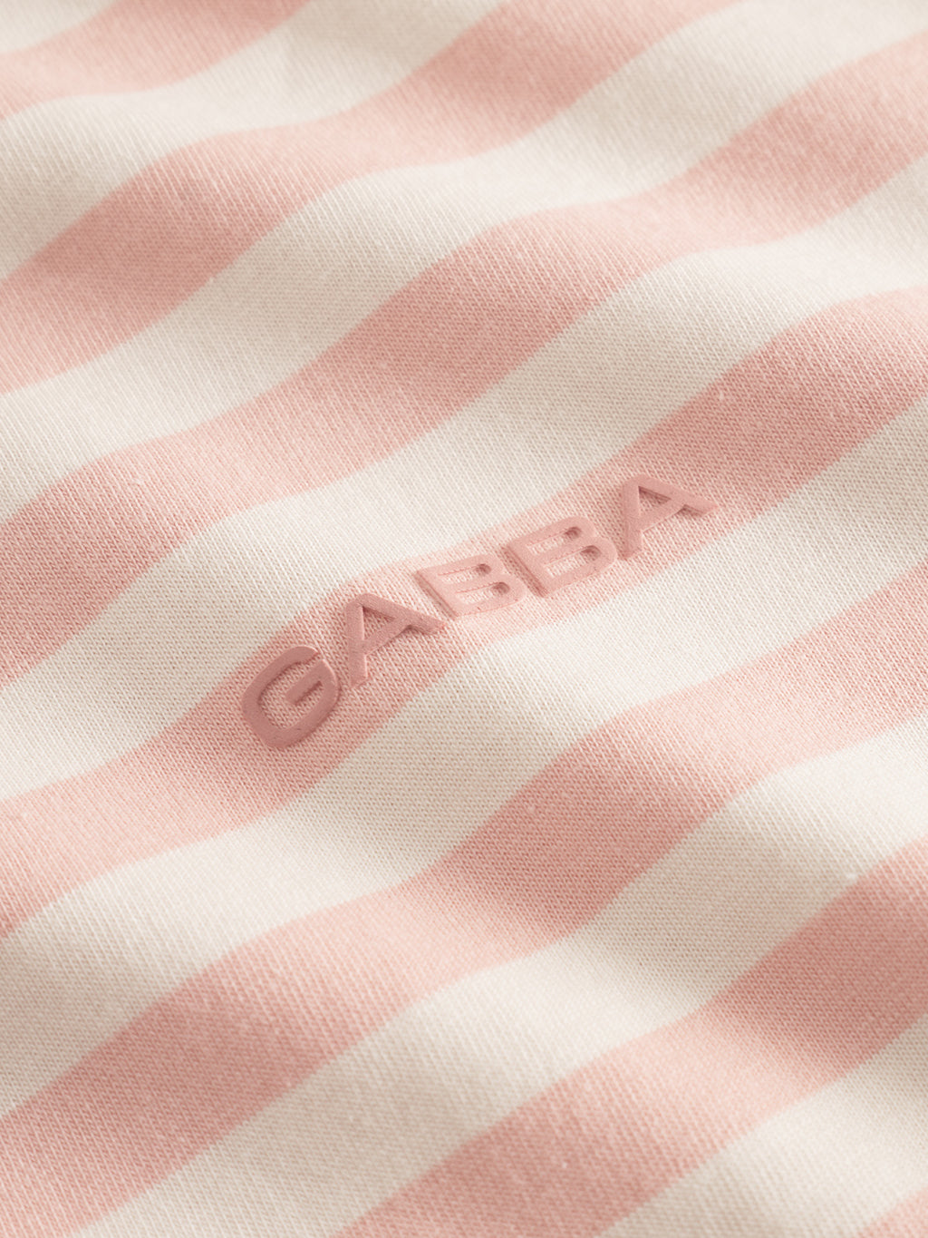 Close-up of white and pink horizontal stripes crafted from organic cotton fabric. The name Gabba is embossed in pink, emphasizing quality. The Dune Logo Stripes SS GOTS - Rose Stripes is a GOTS-certified product.