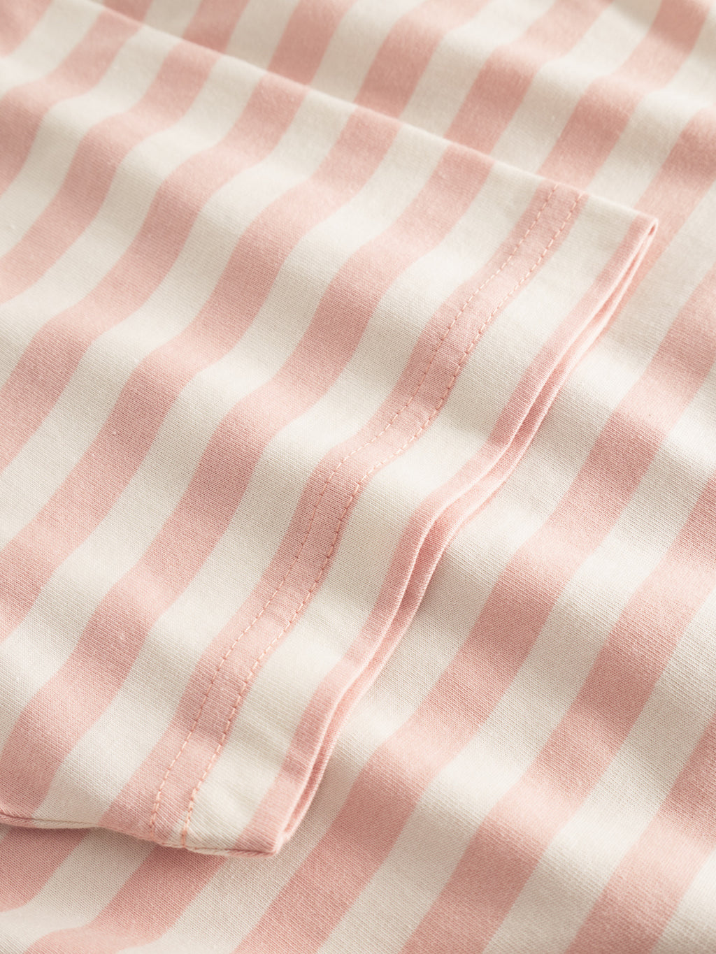 Close-up of Gabbas Dune Logo Stripes SS GOTS - Rose Stripes fabric, featuring pink and white wavy stripes in GOTS-certified organic cotton. The two visible layers have neat edge stitching, with a soft, smooth texture.