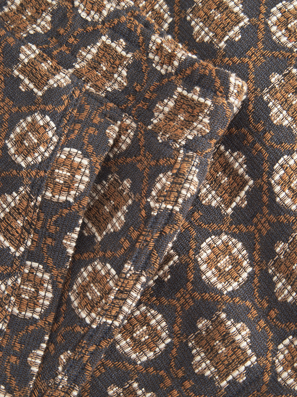 A close-up of Gabbas Fede Box Star shows a fashion-forward design with square and circular geometric patterns in brown, white, and navy, akin to boxy short-and-overshirt sets. The fabric has a soft, slightly crumpled texture.