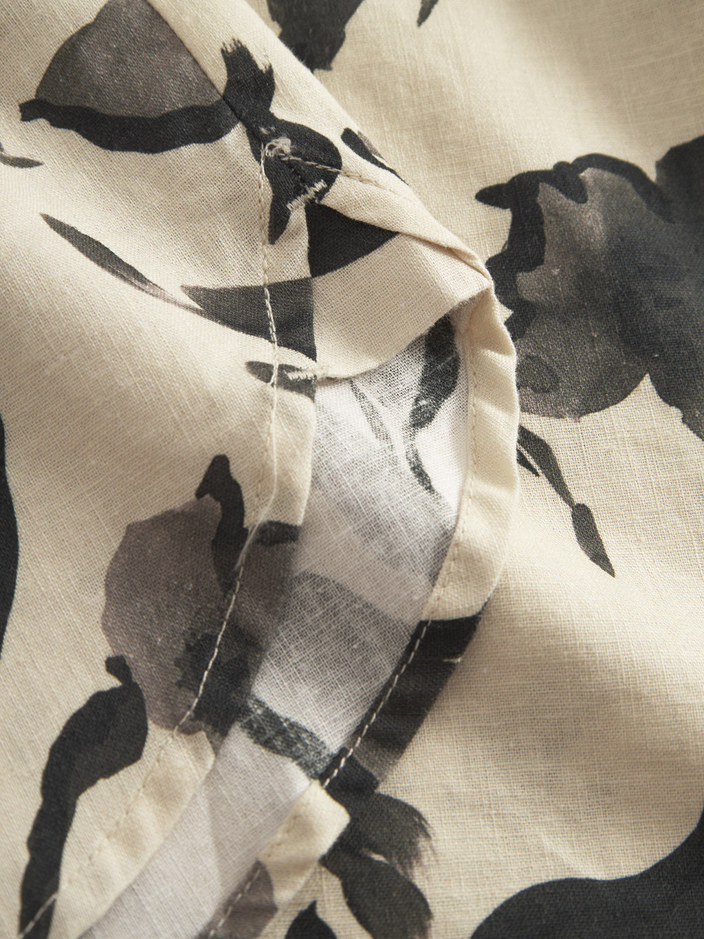 A close-up of the Sven Reg Resort Bloom SS - Meteorite by Gabba showcases premium craftsmanship with a beige fabric featuring abstract black floral patterns, highlighting detailed stitching and high-quality linen in its design.