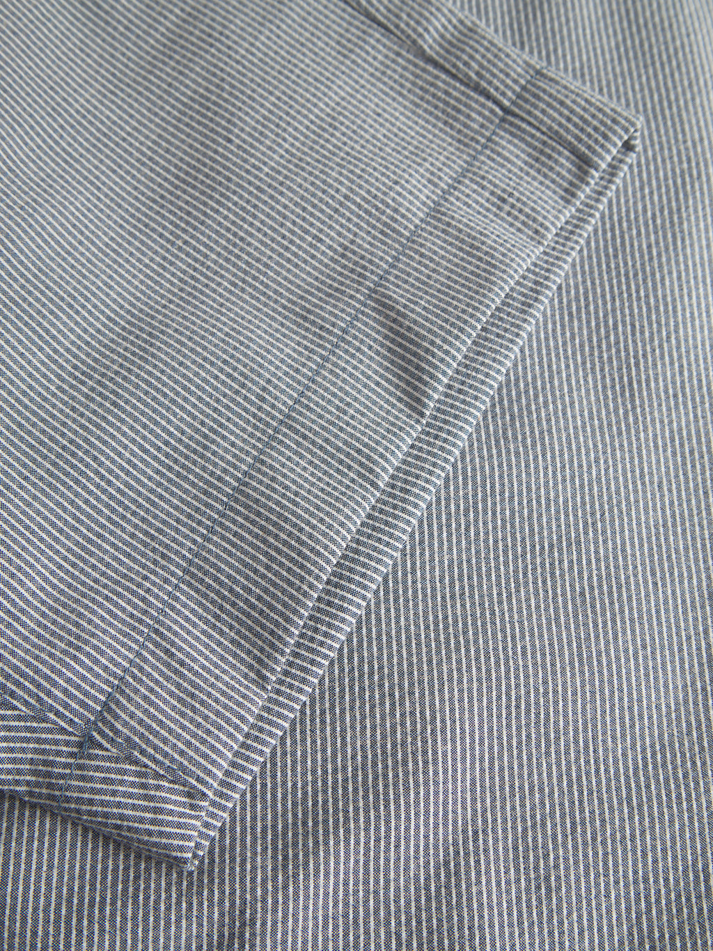 A close-up view of the folded Jet Com2 Shorts - Navy by Gabba reveals a pattern of thin, parallel blue and white vertical stripes. The material, akin to premium shorts, exudes an air of superior comfort and is neatly layered on a similarly designed surface.