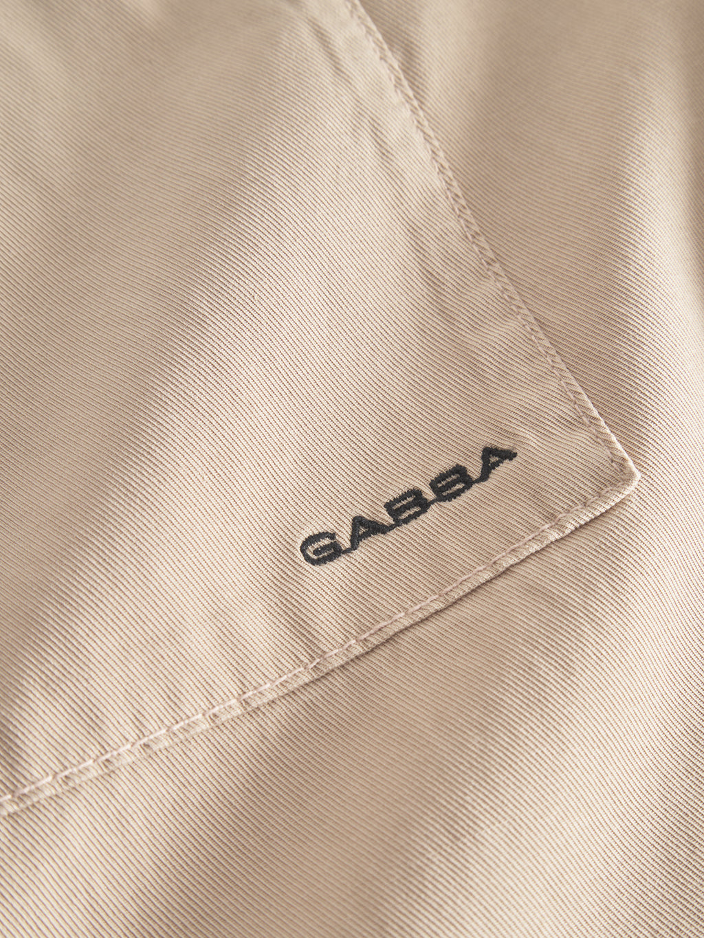 Close-up of the sand fabric from the Gabba Jens Over Lubo LS shirt, revealing a visible seam with Gabba stitched in black. The summer fabrics texture and stitching details exude comfort and are clearly highlighted.