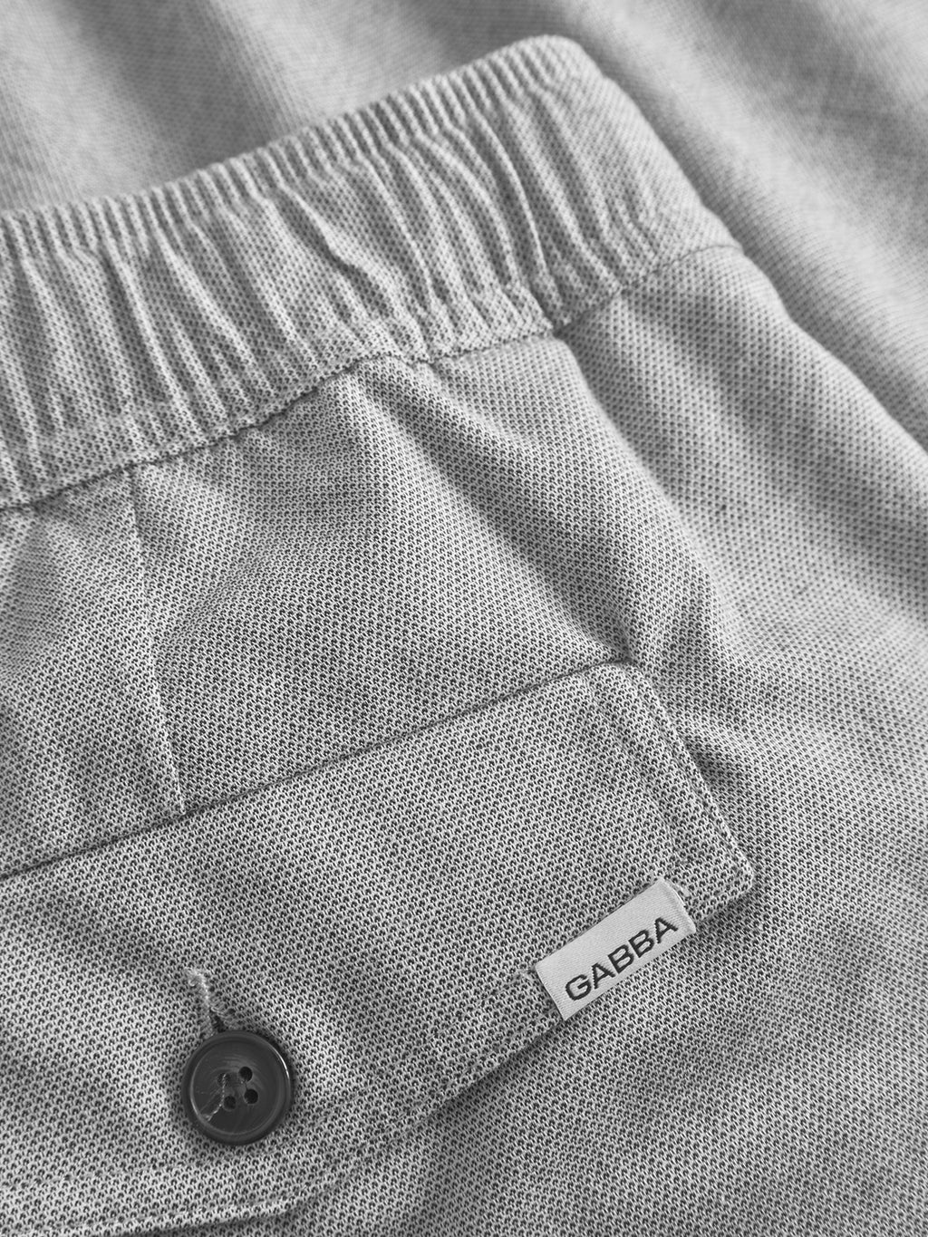 Close-up of Gabbas Coz Belt Carre Shorts in light grey, featuring textured fabric, elastic waistband, buttoned pocket, and a small Gabba label near the pocket for added comfort and style.