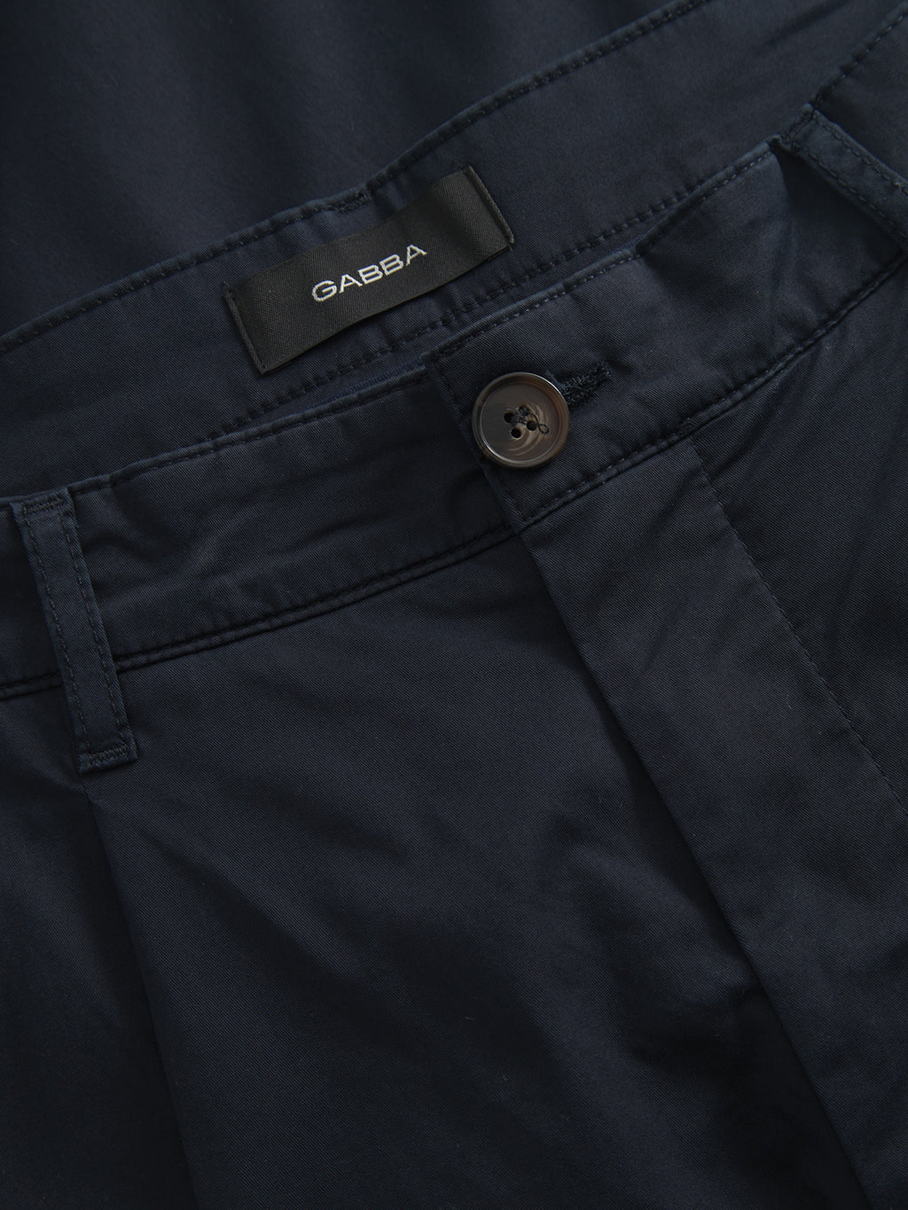 Close-up of the Joe Unite - Navy pants from Gabba, featuring a dark blue color with a brown button and belt loop. The smooth, slightly glossy fabric showcases visible stitching near the waistband, offering a casual look with a subtle tapered leg.