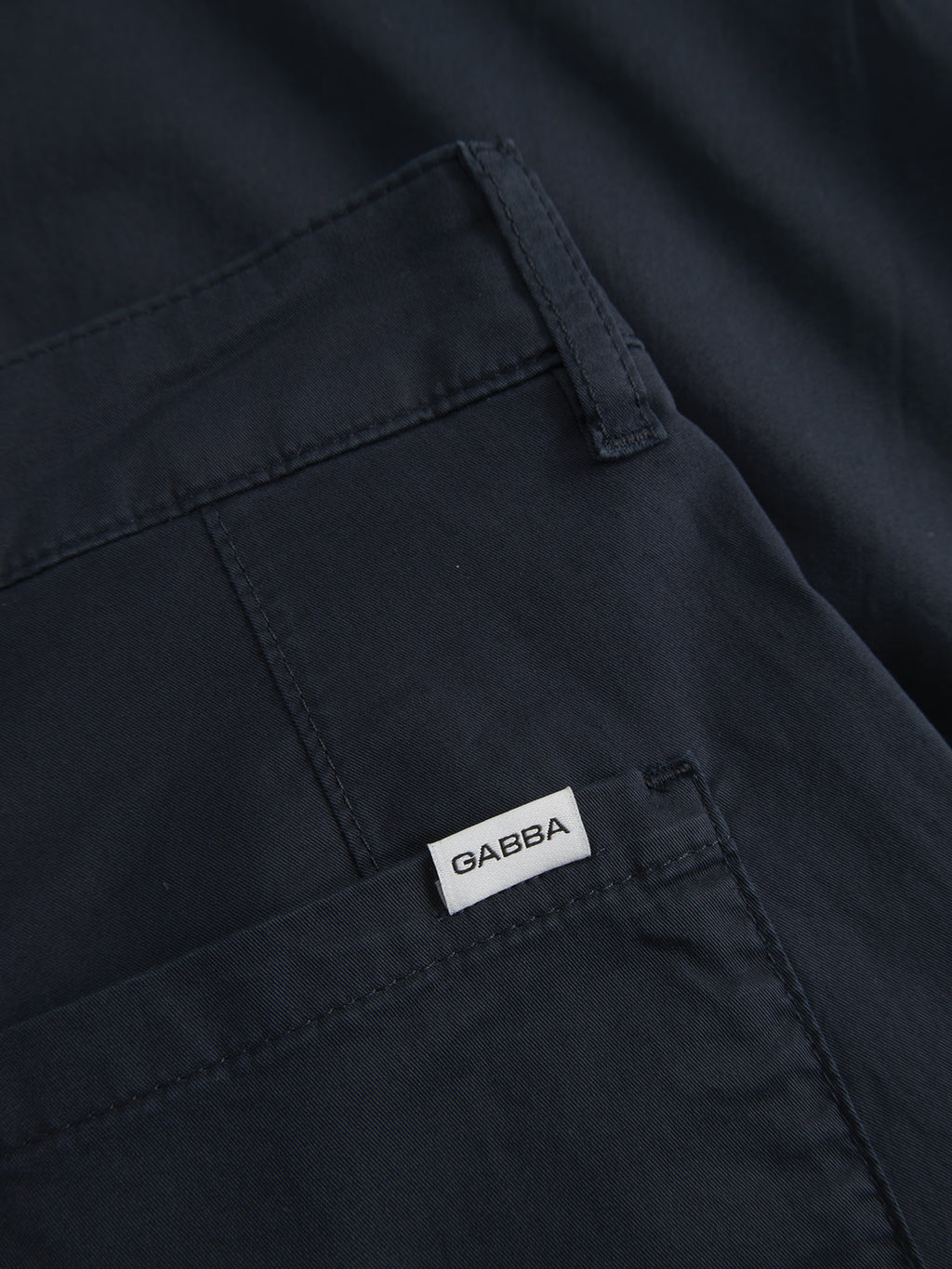 Close-up of navy fabric with visible stitching, exuding a casual look. A small white tag labeled Gabba is sewn near the edge, hinting at its Joe Unite cotton pant origins.