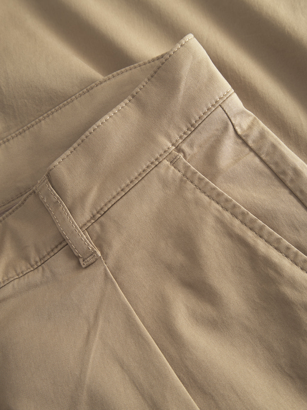 Close-up of the Joe Unite - Sand trousers by Gabba, highlighting the waistband, belt loop, and front pocket. The smooth, well-stitched fabric reflects quality craftsmanship. These relaxed-fit pants offer a casual yet stylish look with their tapered leg design.