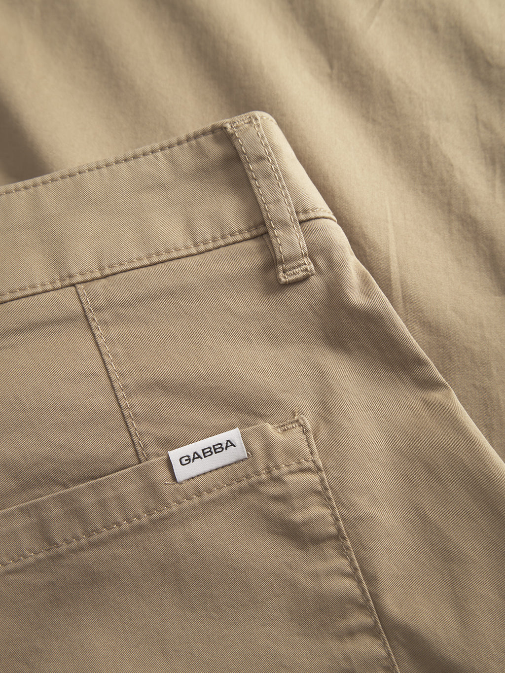 Close-up of Joe Unite - Sand pants by Gabba, featuring a visible back pocket and a small Gabba label. The smooth, tailored fabric highlights stitching details and texture, ideal for a casual look with its relaxed fit and subtly tapered leg.