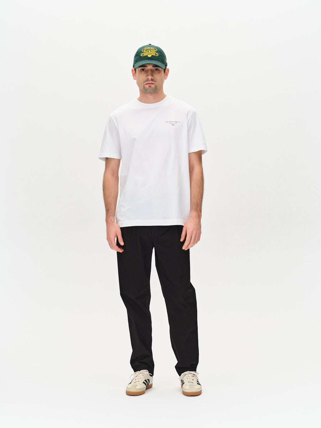 A person in a white T-shirt, relaxed fitted pants, and sneakers stands against a plain white background. They wear the Gabba Joe Unite - Black cap, adding to their casual look.
