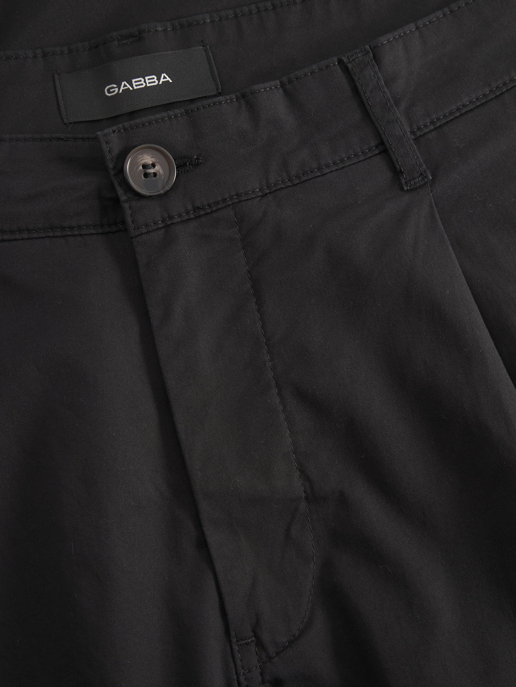 Close-up of Gabbas Joe Unite - Black pants with a waistband, button, buttonhole, and belt loops. The tapered design adds a casual look. Inside the waistband is a Gabba label. The fabric looks smooth and well-tailored.