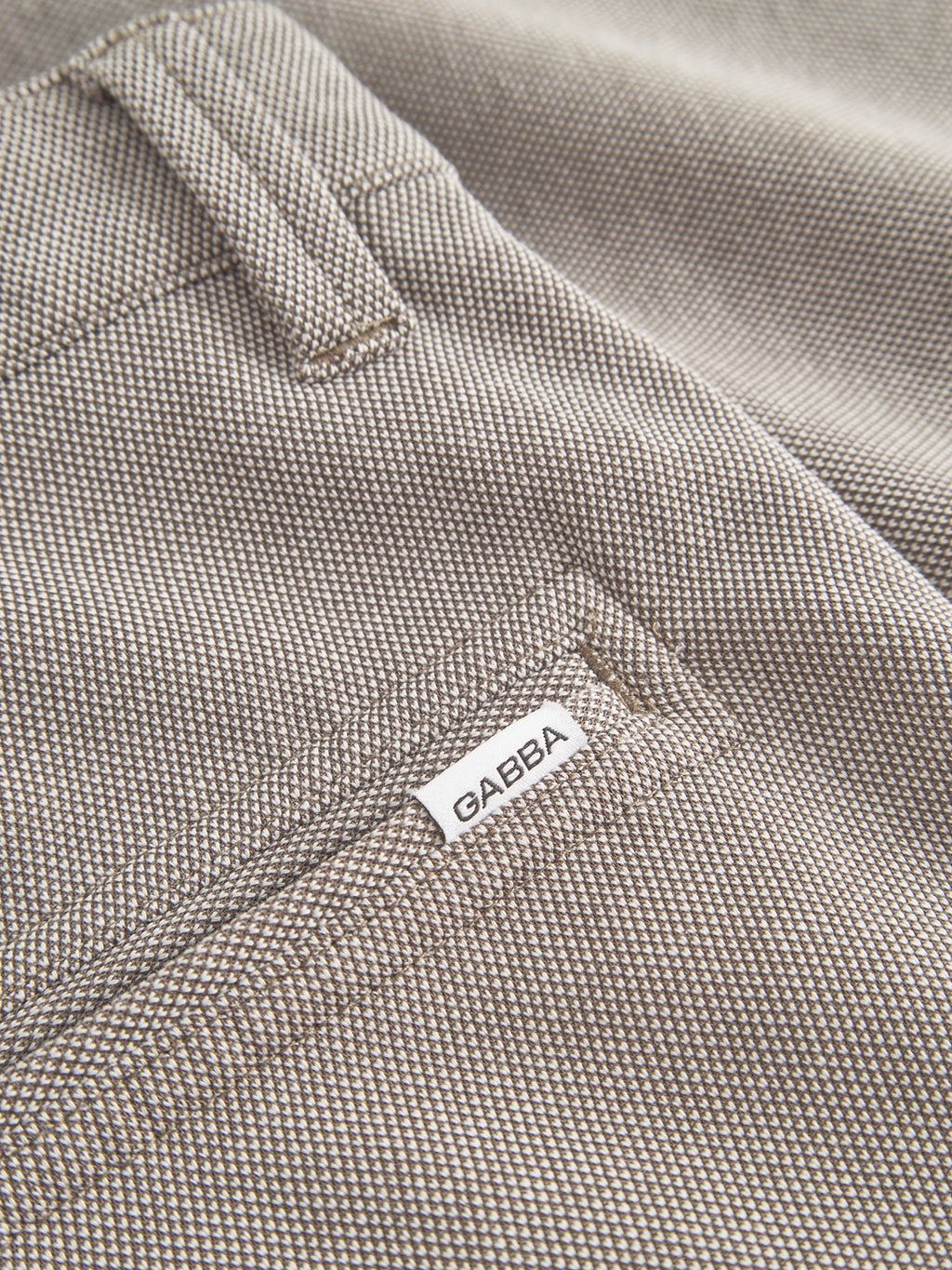 A close-up of textured, durable fabric with a Gabba tag sewn near a seam shows the woven beige and brown pattern of the Jet Tink - Khaki shorts. A visible belt loop hints at superior comfort as part of this premium product.