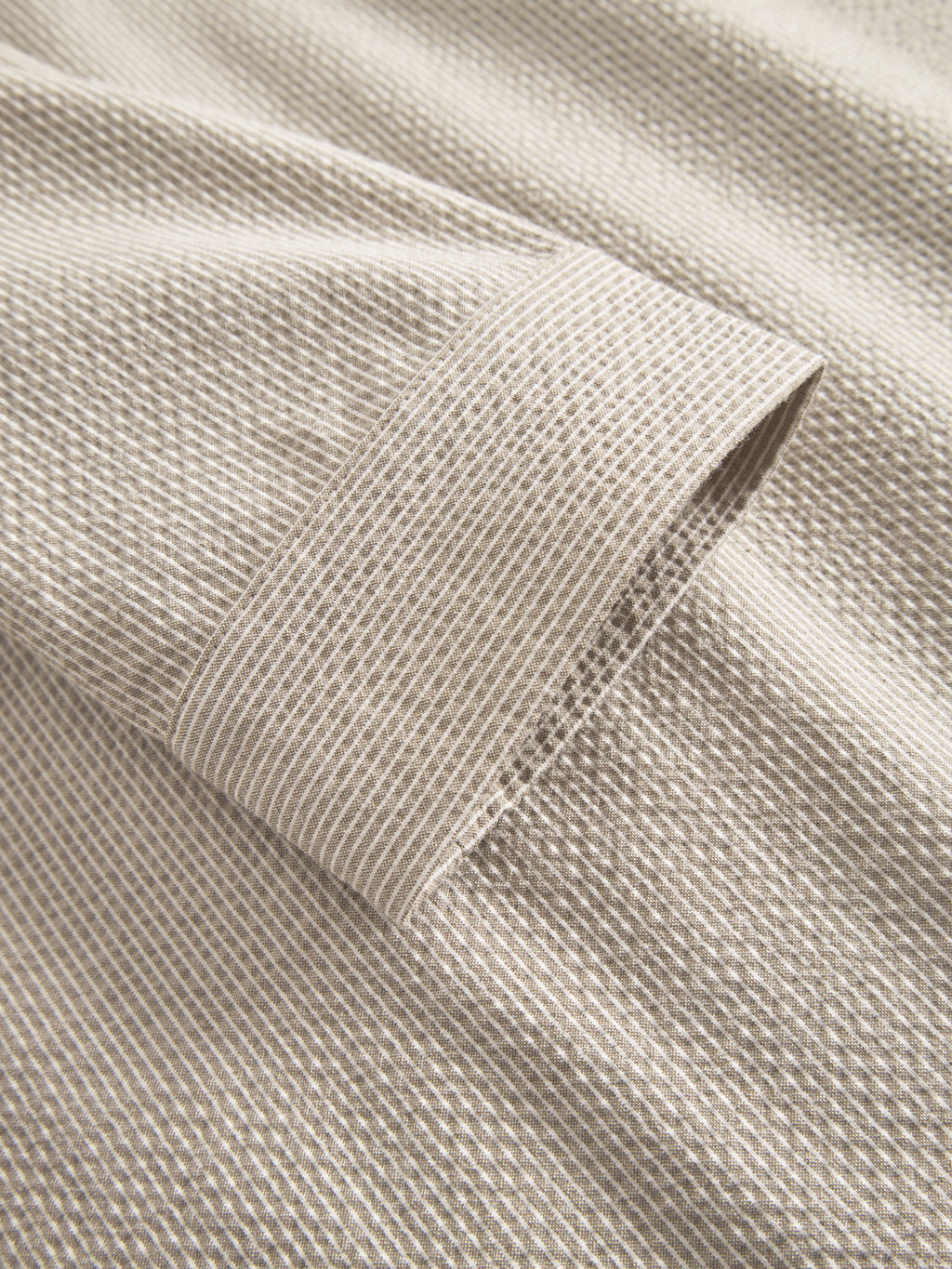 Close-up of Gabbas Today Com2 - Khaki, featuring a beige seersucker fabric with subtle stripes. The image highlights a visible sleeve, showcasing the garments cuff and intricate woven details, emphasizing its soft texture.