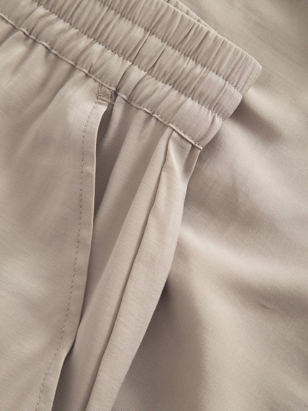 Close-up of Gabbas Bo Yari - Sand Greige pants showcasing an elastic waistband and pleated pocket. The lightweight fabric ensures comfort, while the image highlights the smooth texture, stitching, and intricate details.