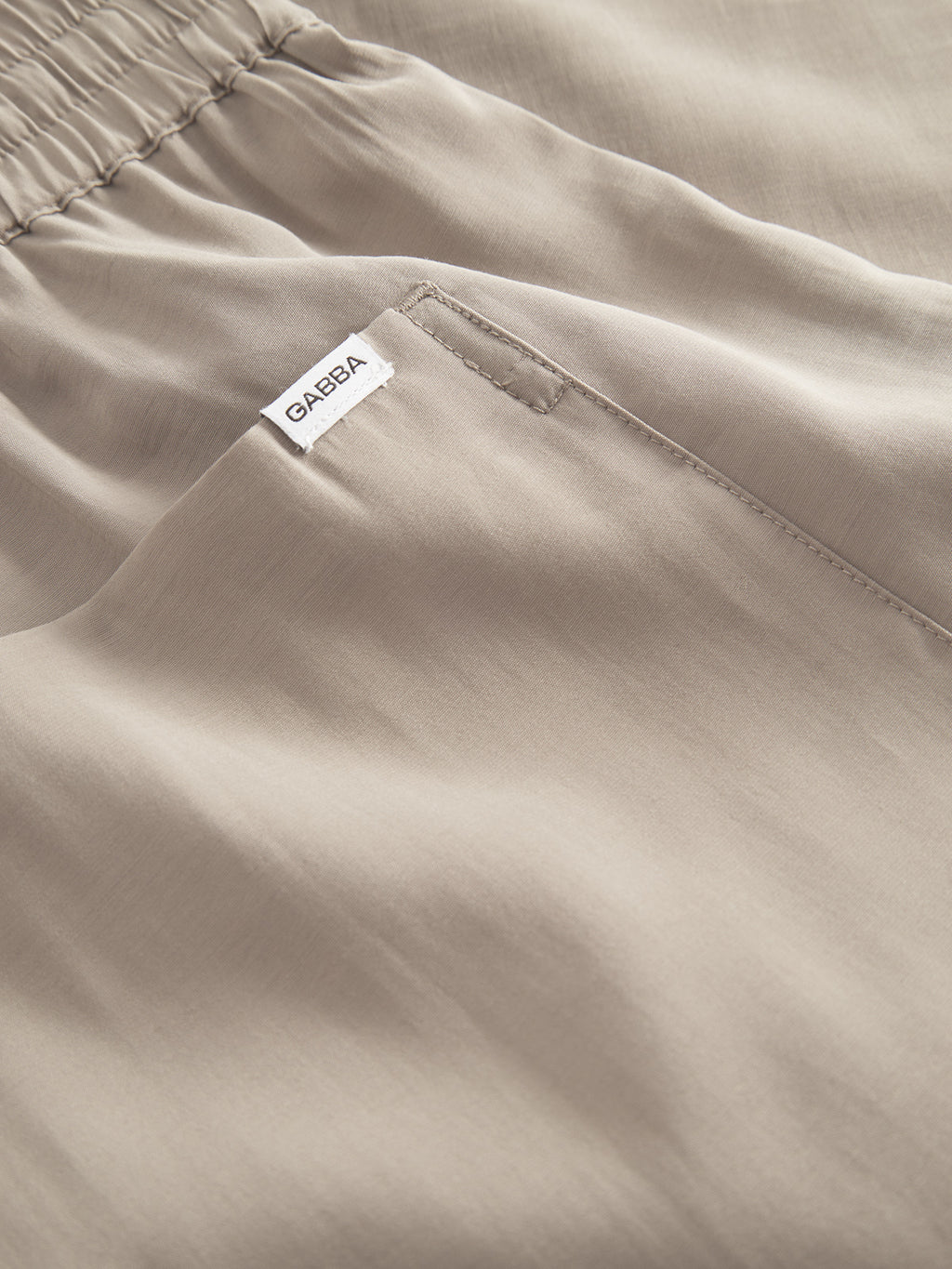 Close-up of Gabbas Bo Yari shorts in sand greige, featuring pocket detail and elastic waistband. A small white Gabba tag is sewn near the pocket. The light fabric provides superior comfort with its smooth, softly textured finish.