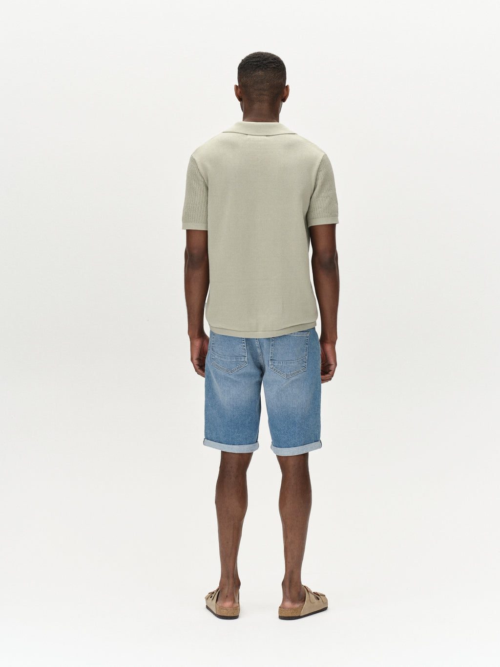 Back view of a person wearing Gabbas Markus 5poc mid-blue denim shorts and a light beige short-sleeve shirt, designed for comfort. Theyre in sandals against a plain white background.