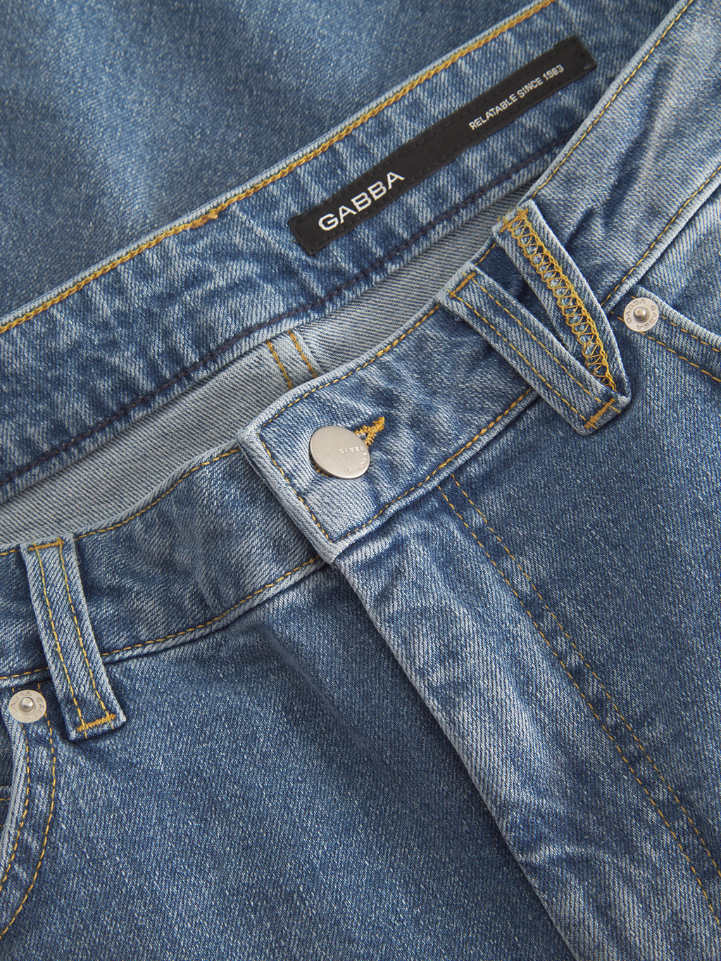 Close-up of Gabbas Markus 5poc - Mid Blue Denim jeans, featuring a metal button and yellow stitching. The black label on the waistband reads Gabba. The fabric texture reveals a classic, eco-conscious look with recycled viscose.