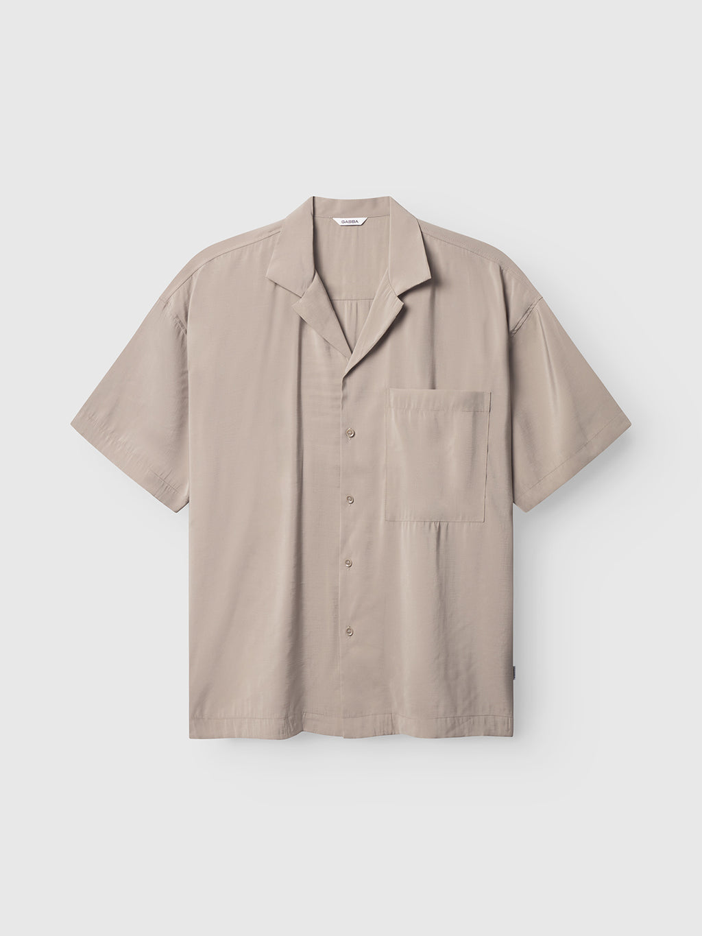 The Gabba Jens Over Resort Yari SS - Sand Greige is a light gray short-sleeve button-up shirt featuring a notched collar and statement chest pocket, presented against a plain white background.