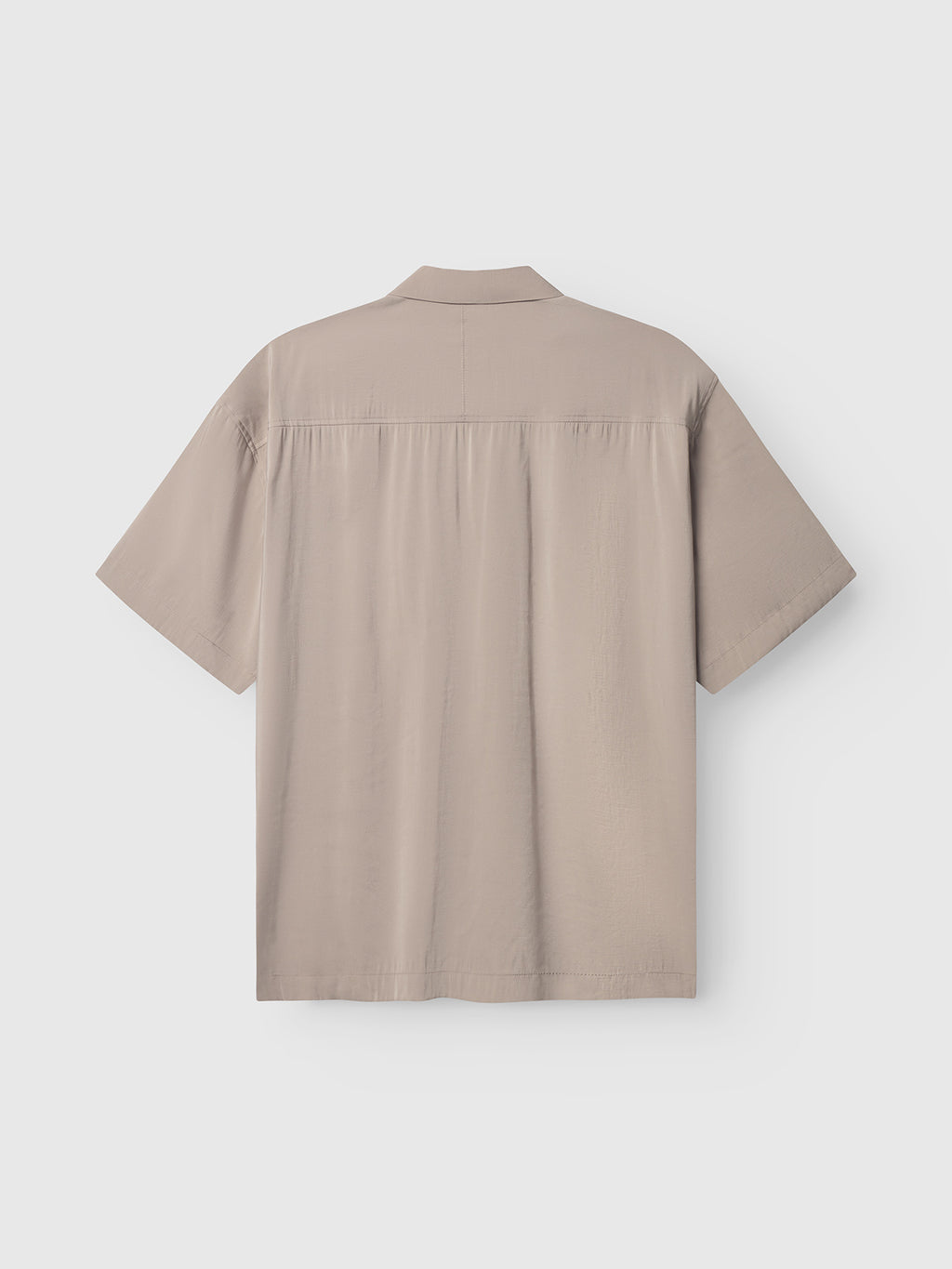 Back view of a Gabba Jens Over Resort Yari SS shirt in Sand Greige. This oversized, beige short-sleeve collared design has a straight hem, upper back seam, and a subtle statement chest pocket for flair. Shown on a white background.