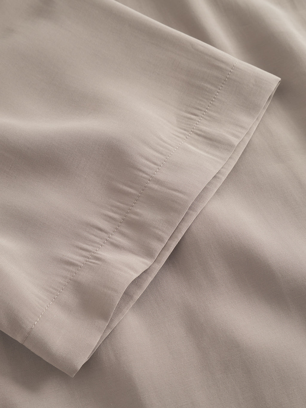 A close-up of the Jens Over Resort Yari SS - Sand Greige by Gabba highlights its smooth, slightly glossy fabric, with visible stitching. Gentle folds and shadows enhance the texture, and fine straight stitching adds to the refined elegance of this premium shirt.
