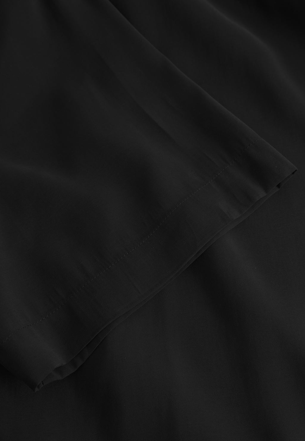 Close-up of the Jens Over Resort Yari SS - Meteorite by Gabba, showcasing a black fabric with a smooth texture. The edge is neatly stitched, and the material drapes naturally with a soft, slightly shiny finish, evoking premium shirt craftsmanship.