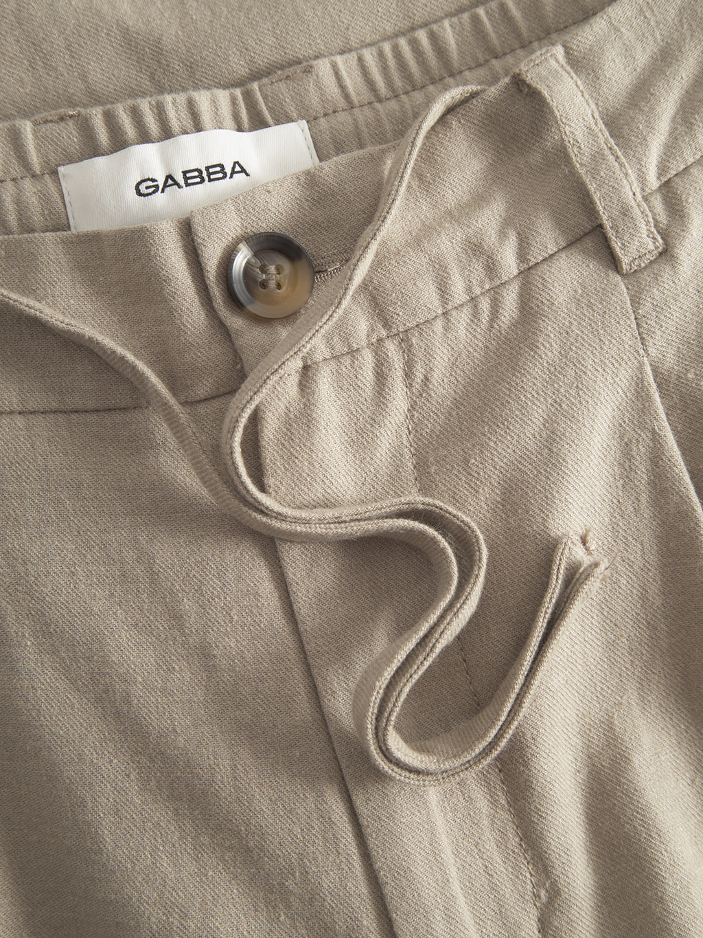 Close-up of the Gabba Napoli 19 Side Lino in Sand Plaza, boasting a relaxed feel with button closure and drawstring. The textured fabric and visible Gabba label inside the waistband enhance its neat stitching for style and comfort.