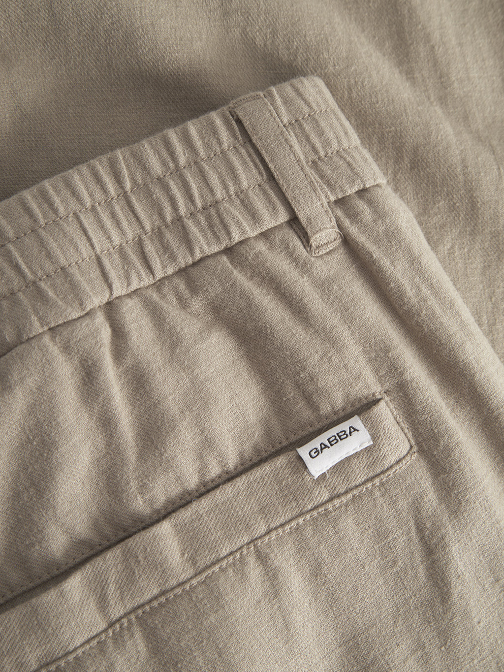 Close-up of Napoli 19 Side Lino - Sand Plaza pants by Gabba in light brown, highlighting an elastic waistband and a pocket with a white Gabba tag. The fabric texture blends style and comfort, offering a relaxed and soft feel.