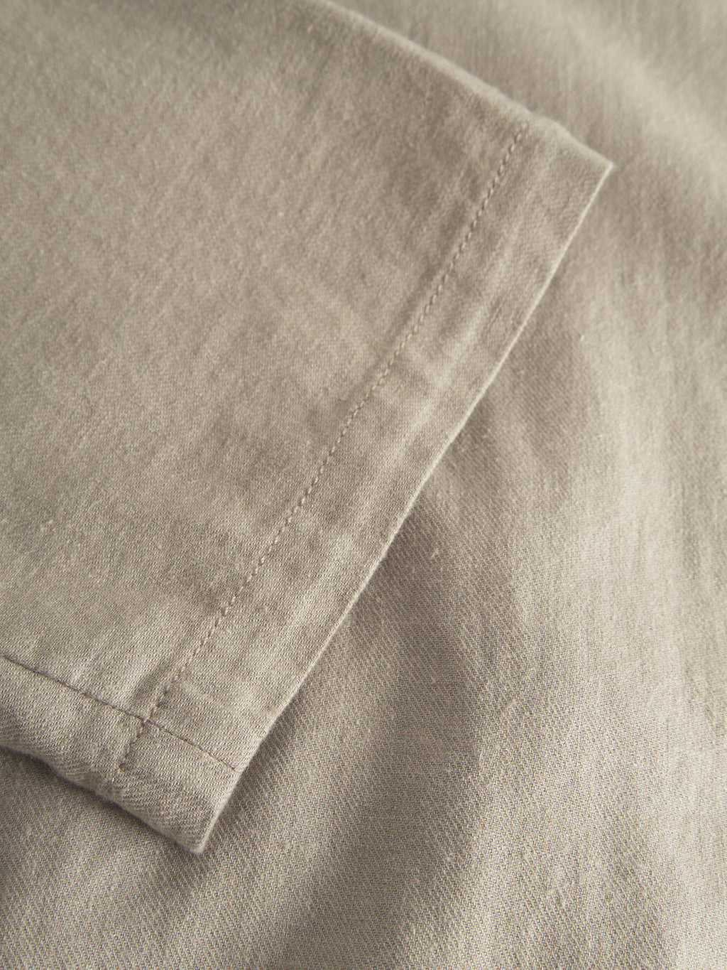 Close-up of a beige fabric with precise stitching and neat seam, reminiscent of the Napoli 19 Side Lino - Sand Plaza by Gabba. The soft texture blends comfort and elegance, exuding a relaxed vibe along the edge.