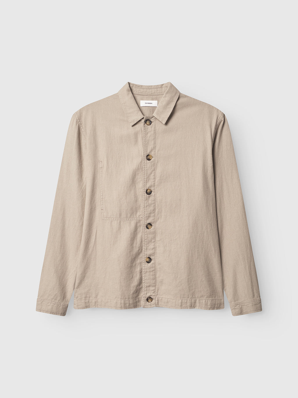 The Gabba Peter Lino - Sand Plaza is a beige linen/cotton button-up shirt, perfect for spring. It has a pointed collar, long sleeves, and a chest pocket. Contrasting brown buttons add style. Displayed against a white background, its ideal as an overshirt.
