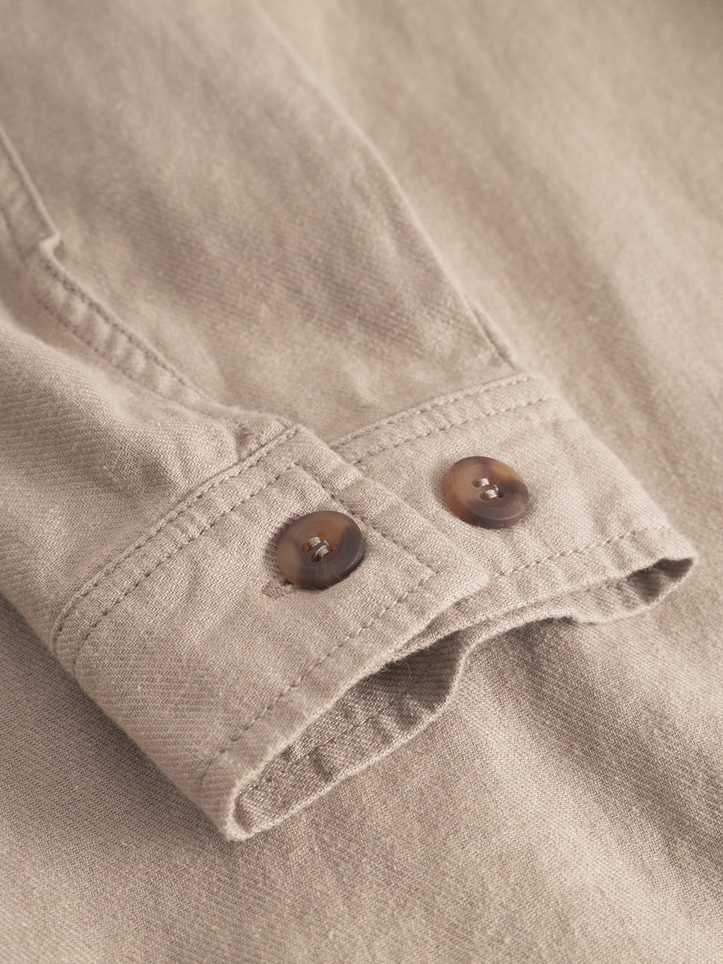 A close-up of the Peter Lino - Sand Plaza sleeve by Gabba showcases a beige linen/cotton blend with two brown cuff buttons. The coarse texture suggests an ideal casual spring overshirt, with visible stitching and button details.