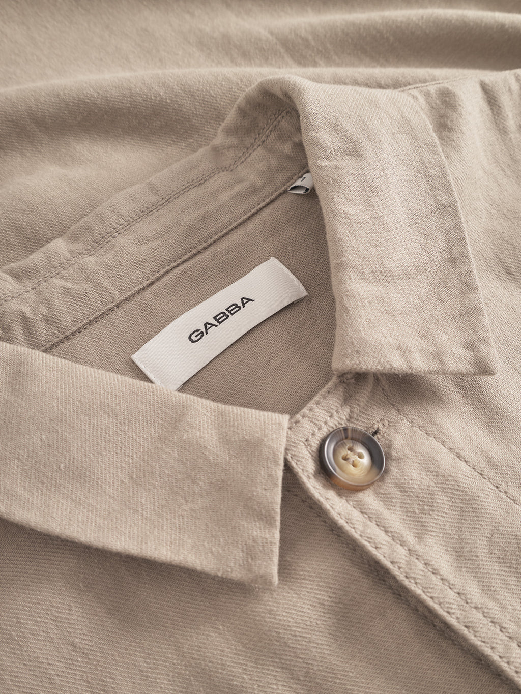 Close-up of the Gabba label inside the collar of the Peter Lino - Sand Plaza overshirt, crafted from textured linen/cotton fabric. Ideal for spring, it features a partially fastened glossy button.