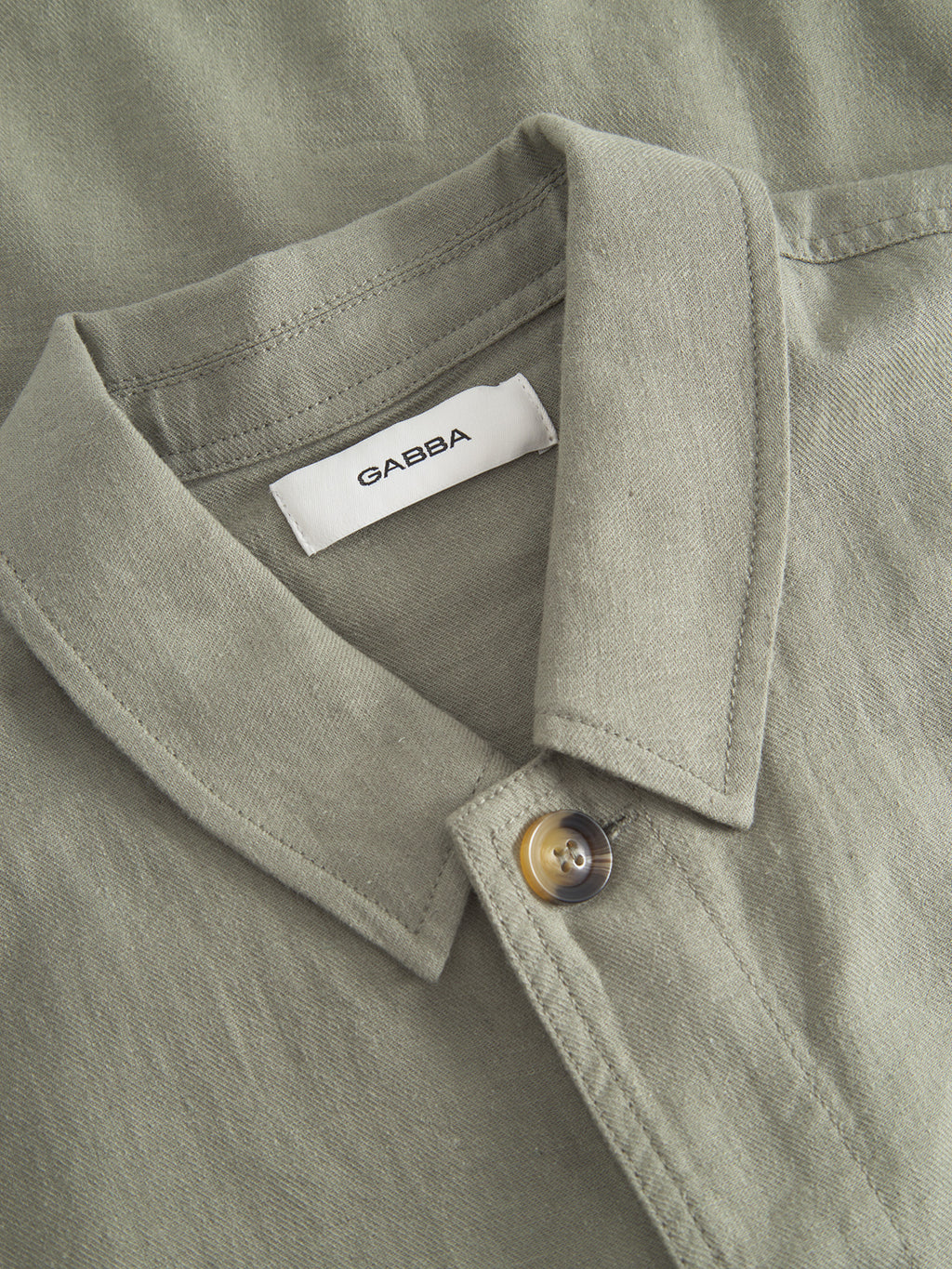 Close-up of a light green GABpeter Lino cotton overshirt by Gabba, featuring a button and a visible white label inside the collar that reads Gabba.