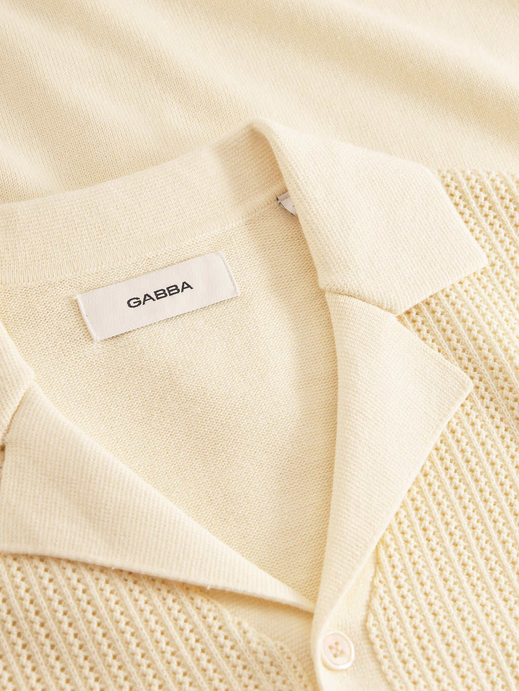 The light beige Geno Resort SS - Ecru Light by Gabba features a textured knit pattern with a retro vibe. The folded collar displays the Gabba label, showcasing its premium quality.