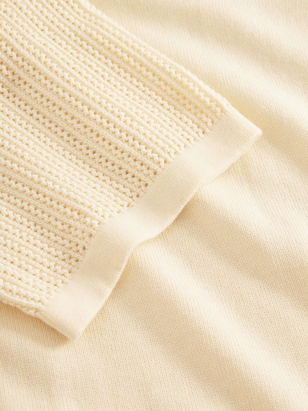 Close-up of the Geno Resort SS - Ecru Light by Gabba showcases its premium knit fabric. The ribbed, textured edge contrasts with the smooth body, reminiscent of a soft, cozy cotton cardigan with intricate stitching.