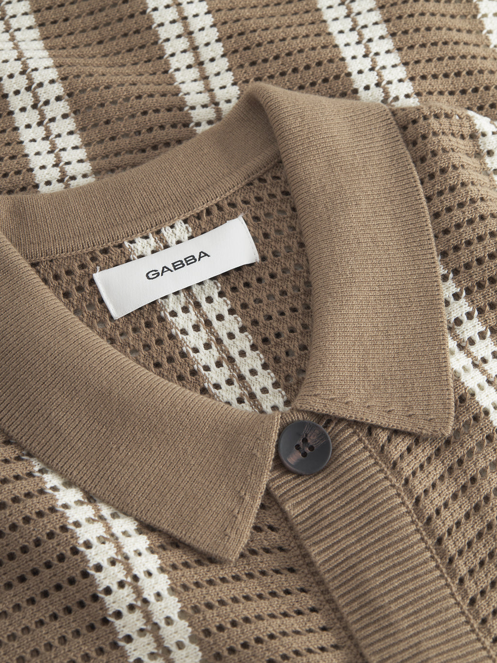 Close-up of the Dezz Stripes LS in brown stripe by Gabba. This knitted sweater, made from soft cotton, features a textured perforated pattern with vertical stripes and a buttoned collar.