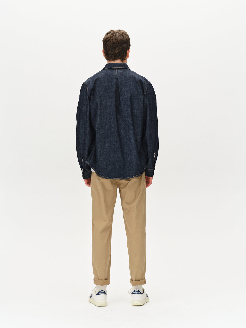A person with short brown hair is seen from the back, wearing a Gabba Jap Beam - Dark Blue Denim shirt, beige pants, and white sneakers against a plain white background.