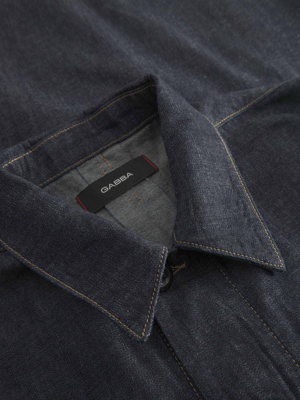 Close-up of the Jap Beam - Dark Blue Denim shirt from Gabba, featuring dark selvage fabric, yellow stitching, and a pointed collar. The visible GABBA tag attests to its quality. Part of the exclusive Loomers project capsule, this 100% cotton piece highlights fine texture and design details.