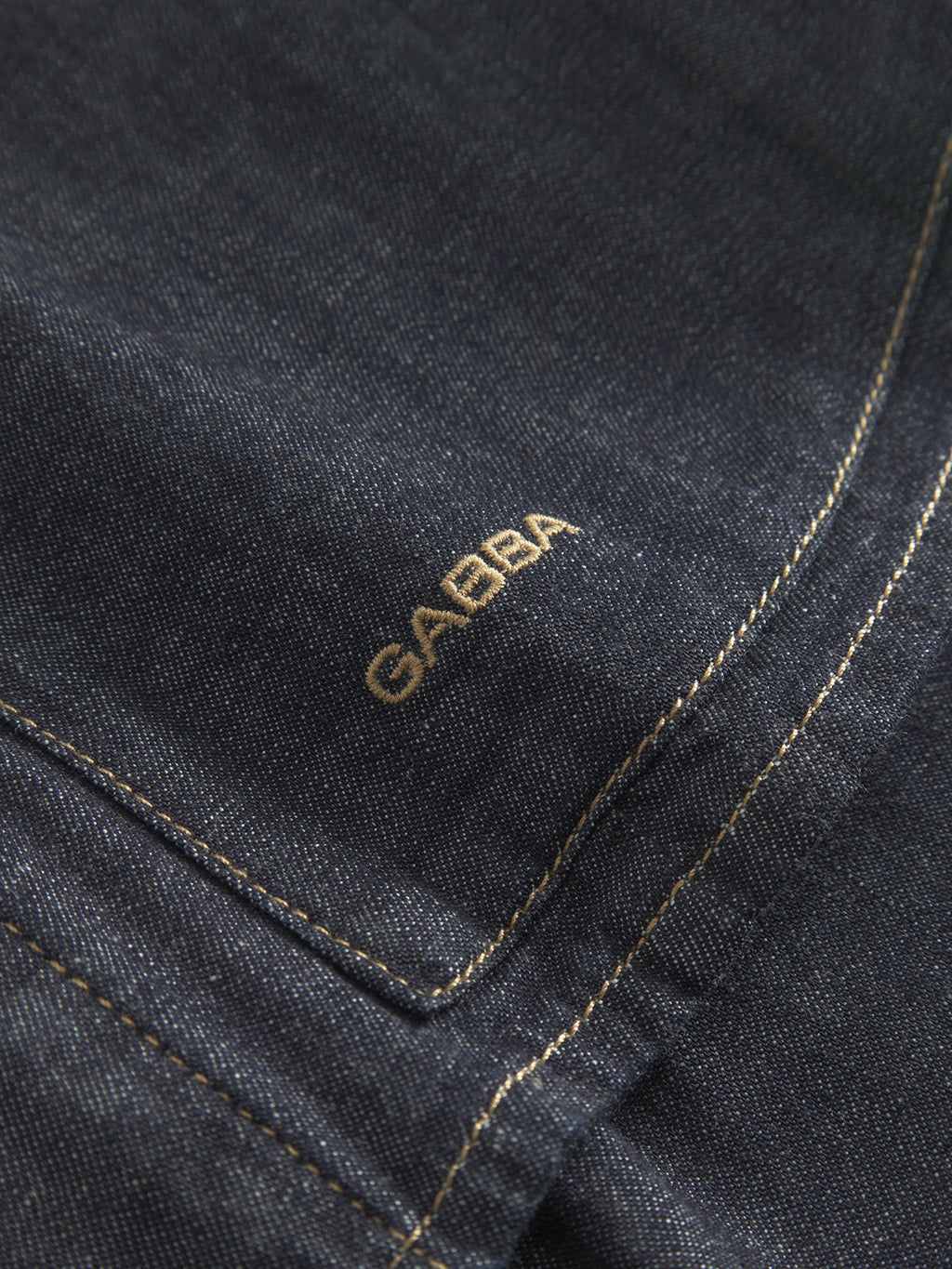 Close-up of Jap Beam - Dark Blue Denim by Gabba, featuring dark denim fabric with yellow stitching made from 100% cotton. The word GABBA is embroidered near the seam in gold thread, showcasing artistry like a Loomers project capsule.
