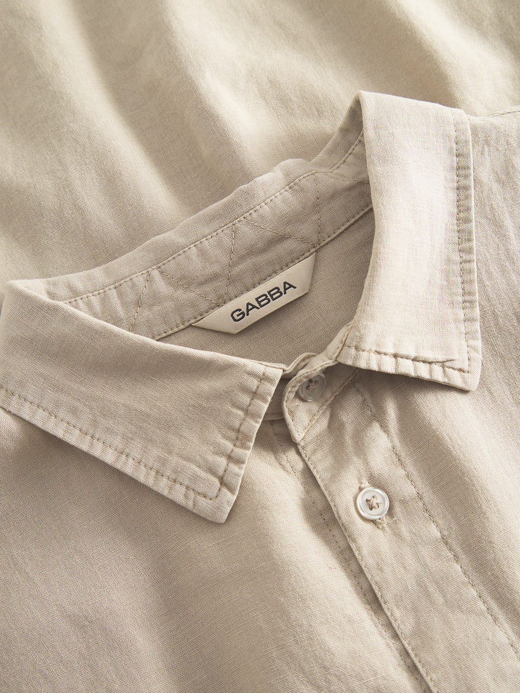 Close-up of a Sand Plaza premium shirt, Sven Reg Lino SS by Gabba, featuring a collar and one visible button. The soft, lightweight fabric exudes comfort with the Gabba label inside the collar.
