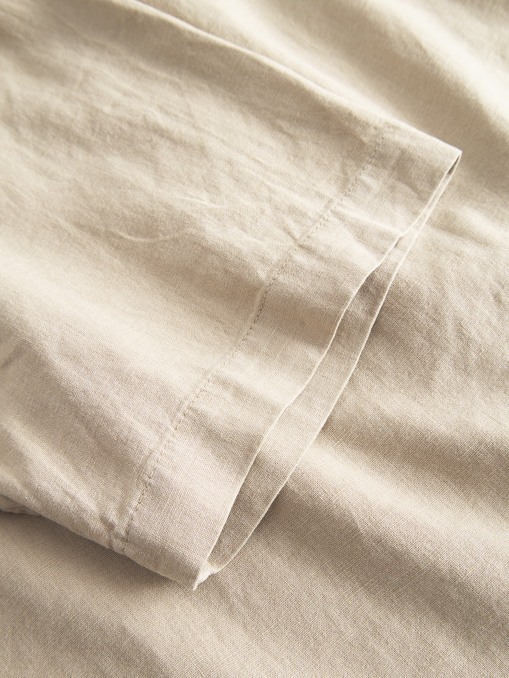Close-up of the Sven Reg Lino SS - Sand Plaza shirt by Gabba, highlighting its beige linen fabric with texture and seam detail. The soft, lightweight material has visible stitching on the folded edge, showcasing a smooth surface and subtle sheen for ultimate comfort.